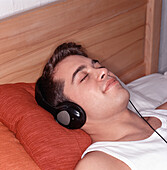 Mann auf dem Bett liegend, mit Kopfhörern