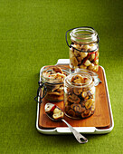 Preserved Mushrooms in Jars with Spoon on Wooden Cutting Board and Tray on Green Background in Studio