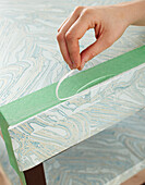 Close-up of Woman's Hand Applying Wallpaper to Table in Studio