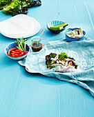 Rice Wrap on Blue Table Cloth with Bowls of Ingredients on Blue Wooden Table in Studio