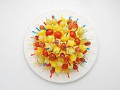 Appetizer picks with cheese and fruit displayed in a ball shape on paper plate, on white background, studio shot