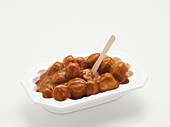 Currywurst mit Holzgabel in Plastikbehälter, auf weißem Hintergrund, Studioaufnahme