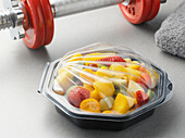 Fruit salad in plastic container with barbell, studio shot