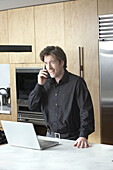 Man with Laptop and Cellular Phone in Kitchen