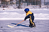 Kleiner Junge spielt Hockey auf einem zugefrorenen Teich, Fuschlsee, Salzburger Land, Österreich