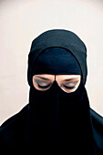 Nahaufnahme einer jungen Frau, die einen schwarzen muslimischen Hijab und ein muslimisches Kleid trägt, mit geschlossenen Augen und Augen-Make-up, Studioaufnahme auf weißem Hintergrund