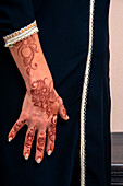 Woman standing indoors, with close-up of arms and hand painted with henna in arabic style, wearing a typical black, arabic, muslim dress, studio shot