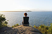 Rückenansicht einer Frau, die auf einem Hügel sitzt, Ilha do Mel, Parana, Brasilien