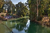 Bäume, die sich im Fluss spiegeln, mit am Ufer versammelten Menschen