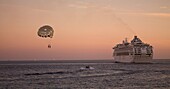 Kreuzfahrtschiff und zwei Personen mit Fallschirm über dem Meer, Dämmerung; Los Cabos, Mexiko