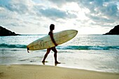 Mann trägt Surfbrett am Strand; Mexiko