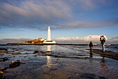 Vater mit zwei Kindern, die einen Leuchtturm beobachten; Whitley Bay, Northumberland, England