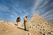 Ein Führer, der ein Kamel und einen Passagier bei den Pyramiden führt