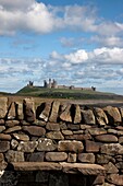 Rustikale Steinmauer mit Burg Dunstanburgh, England, Northumberland