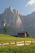 Kastelruth, Südtirol, Italien; Zaun und Scheune auf einer Wiese mit Bergen im Hintergrund