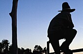Silhouetted Cowboy Leaning Against Fence