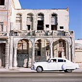Classic White Car Passing Rundown Building