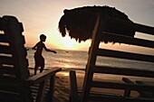 Silhouetted Boy Walking By Deckchairs And Umbrella