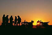 Fünf Silhouetten von Menschen auf Quad-Bikes bei Sonnenuntergang