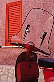 Roter Motorroller vor einer rosa Wand, Nahaufnahme