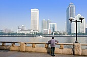 Man Standing By River With Guangzhou Business District In Background