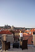 Frau lehnt auf einer Dachterrasse und blickt über das Prager Stadtbild