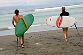 Zwei Frauen tragen Surfbretter zum Meer