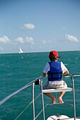 Boy In Life Vest Sitting On Edge Of Sailboat