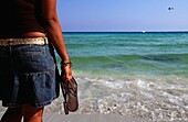 Mädchen mit Sandalen am Strand stehend, Zypern