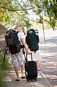 Junges Paar geht mit Rucksack und Koffer die Straße entlang