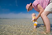 Mutter und Baby in seichtem Wasser vor dem Strand, Blickwinkel niedrig