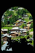 Blick durch ein gewölbtes Fenster auf Alpenhütten und Chalets am Berghang