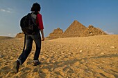 Woman With Rucksack Walking Towards Pyramids At Dusk