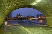 Archway Under Bridge Looking Towards Notre Dame Cathedral At Dusk.