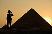 Silhouette einer Frau beim Fotografieren der Pyramiden in der Abenddämmerung