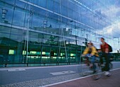 Two Women Cycling Past Modern Architecture, Blurred Motion