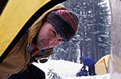 Mann schaut in Zelt beim Camping in einem Schneesturm
