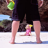 View Through Father's Legs Of Child Playing In The Sand