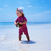 Kind watet im Wasser und hält Seegras