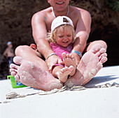 Child Sitting On Her Fathers Lap On The Beach