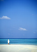 Frau in Weiß am Rande eines tropischen Strandes stehend