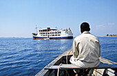 Mann im Boot mit Ilala-Dampfer im Hintergrund auf dem Nyasa-See