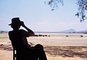 Silhouette einer Frau, die Elefanten neben einem See im Vwaza Marsh Wildlife Reserve beobachtet