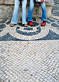 Two Teenagers Sitting On A Beach, Tiles In Foreground