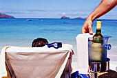 Mann im Liegestuhl wird am Strand von einem Kellner mit Wein bedient