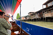 Männlicher Tourist filmt Häuser vom Longtailboot auf dem Klong Bangkok Noi
