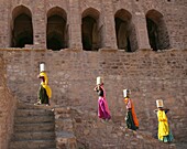 Women In Colorful Saris Carrying Boxes On Their Heads While Climbing Stairs