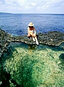 Frau sitzt bei Felsenpools mit Meer im Hintergrund