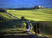 Blick über die Straße in der Abenddämmerung zum alten Bauernhaus auf einem Hügel in der Nähe des Dorfes Pienza