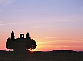 Zypressen neben einer kleinen Kapelle in der Abenddämmerung bei San Quirico D'orcia